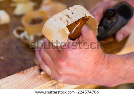 Carpenter working with a wood planer on workpiece in his workshop or carpentry
