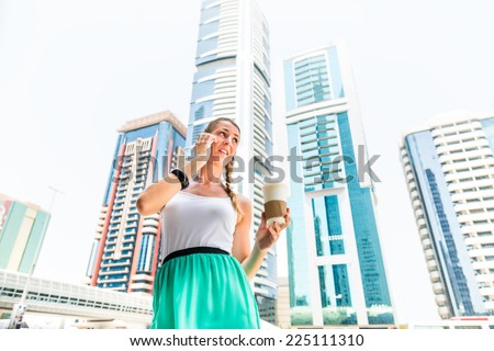 Young woman telephoning with mobile phone, drinking coffee in metropolitan city Dubai