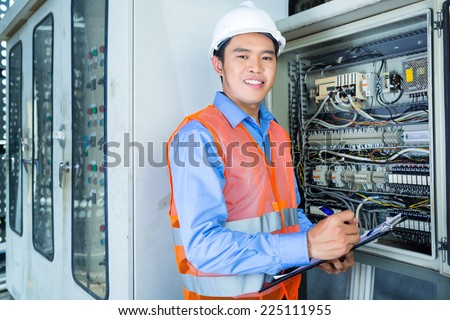 Asian Indonesian Technician or electrician making function test on breaker box or switchbox with power lines on construction site or in factory for acceptance