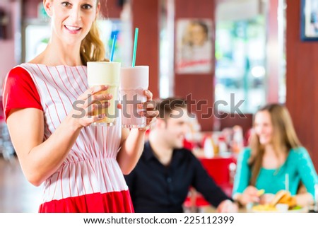 Friends or couple eating fast food and drinking milk shakes on bar in American fast food diner, the waitress wearing a short costume