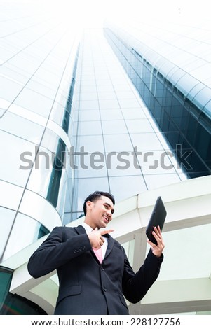 Asian businessman checking outside mails on tablet computer in front of tower building