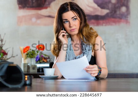 Young woman on the phone in a cafe or restaurant, she discusses some documents