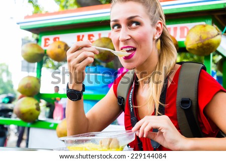 European Woman eating at mobile kitchen stall on Jakarta travel exploring Indonesia street food