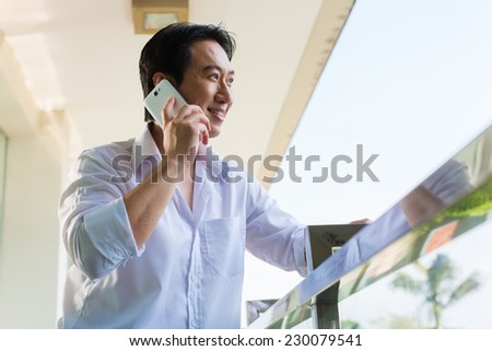 Asian man telephoning on home balcony with smartphone