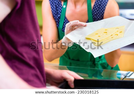 Saleswoman at organic supermarket counter offering customer cheese