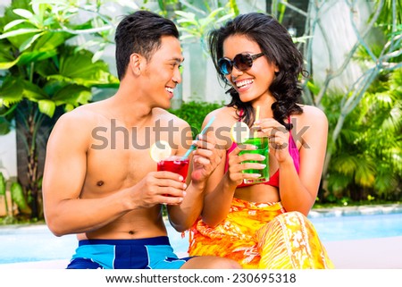 Asian couple drinking fancy cocktails at hotel or club pool