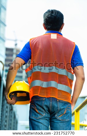 Asian Indonesian construction worker with helmet and safety vest on a building site in Asia