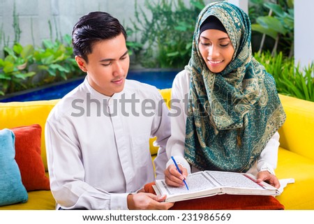 Asian Muslim man teaching woman reading Koran or Quran in living room
