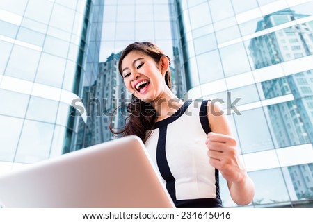 Asian businesswoman working on laptop in front of tower building