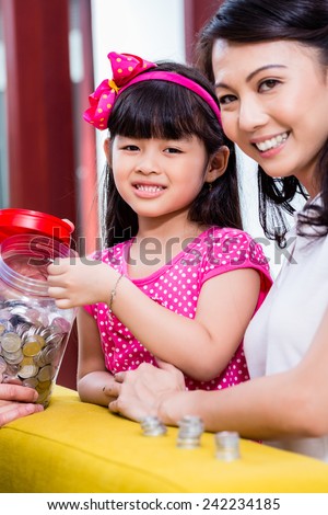 Chinese family saving money for college fund of child, putting coins in jar