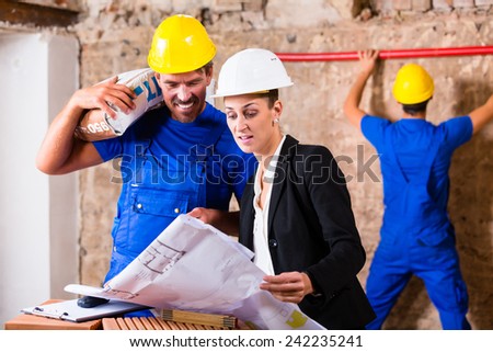 Architect and construction worker having sack of cement on shoulder on site with plan