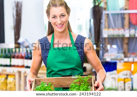 Organic Supermarket shop assistant filling up herbs storage racks in vegetable department