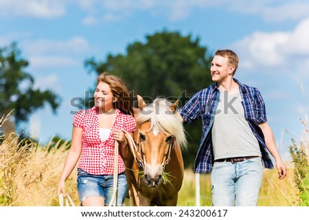 Couple leading horse thru summer meadow