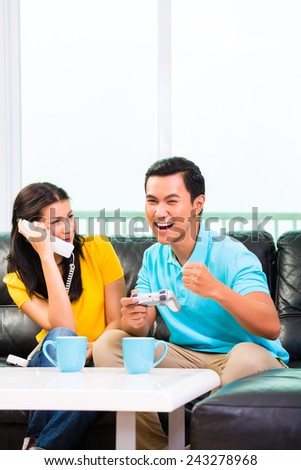 Young Asian handsome couple having leisure time together and playing with laptop video game console and phone on couch