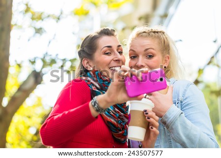 Women friends with coffee and phone walking down street in city