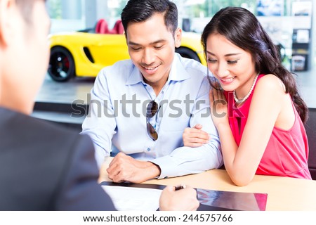 Asian Couple signing sales contract for car at dealership