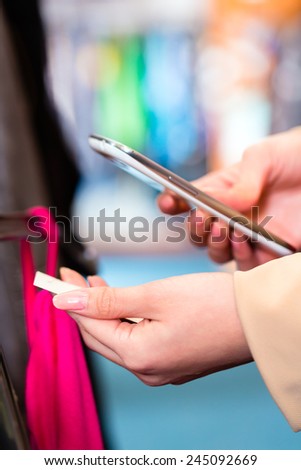 Woman shopping in boutique or fashion store comparing prices with mobile phone scanning the price tag