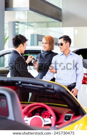 Asian couple buying car in auto dealership consulting the salesman
