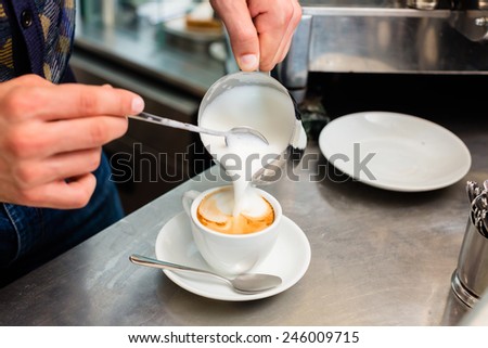 Barista in cafe or coffee bar preparing proper cappuccino pouring milk froth in a cup