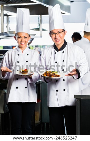 Asian Indonesian chef along with other cooks in restaurant or hotel commercial kitchen cooking, finishing dish or plate
