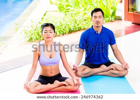 Asian yoga couple in lotus seat mediating in their tropical home in front of garden