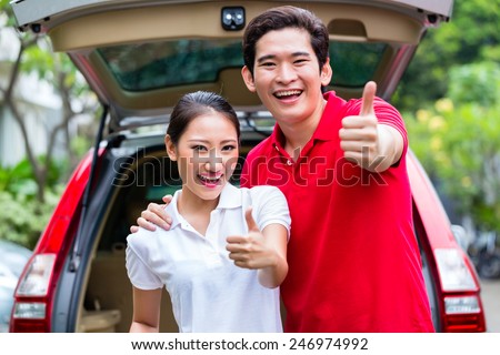Asian couple loading suitcase for travel in luggage trunk of car