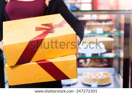 Woman presenting cake and pastries in takeaway boxes in cafe or pastry shop