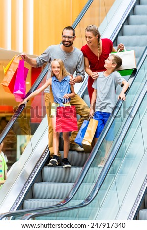 Family in shopping mall on escalators with bags