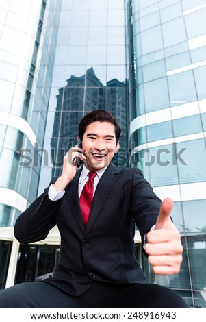 Asian businessman telephoning with smartphone in front of tower building