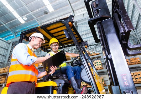 Asian fork lift truck driver discussing checklist with foreman in warehouse