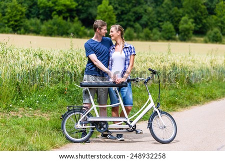 Man and woman, a couple,  riding together tandem bike on country lane