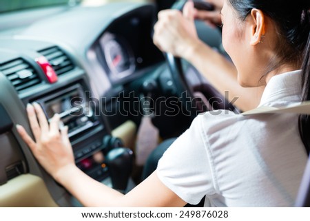 Asian couple driving new car, she is turning on the radio