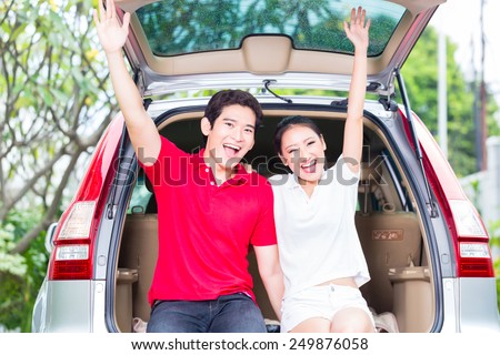 Asian couple buying new car, cheering and sitting in luggage trunk