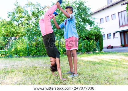 Brother and sister, two black children, playing in garden doing handstand