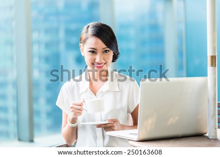 Chinese Business woman drinking coffee sitting in front of laptop on terrace in front of city skyline