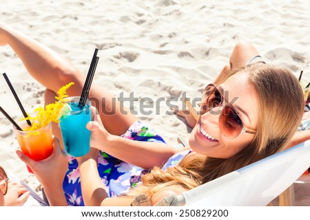 Two girls or woman drinking cocktails in beach club and sitting on sun lounger