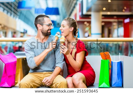 Couple eating ice cream in shopping mall with bags