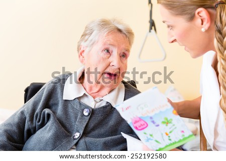 Nurse giving birthday card to senior woman in nursing home sitting in wheelchair