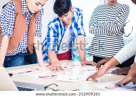 Advertising agency team choosing model for campaign among pictures spread out on table