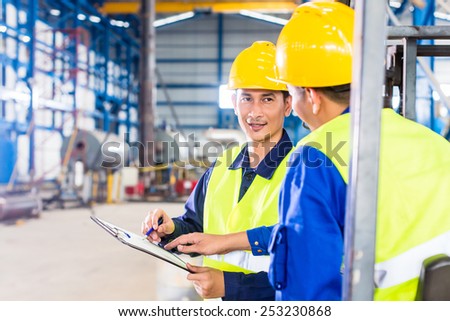 Worker and forklift driver in industrial factory looking at camera