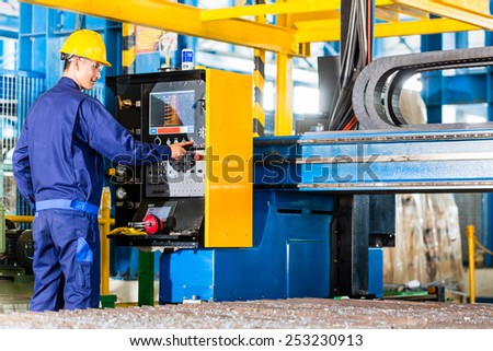 Worker in manufacturing plant at CNC machine control panel