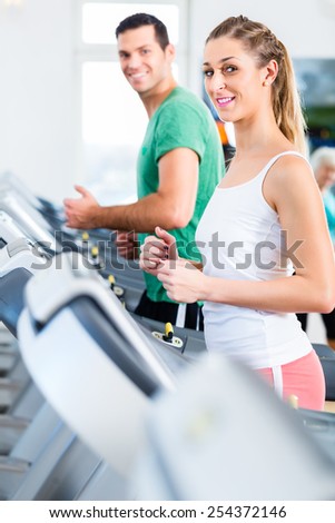 Couple on treadmill in fitness gym running for sport