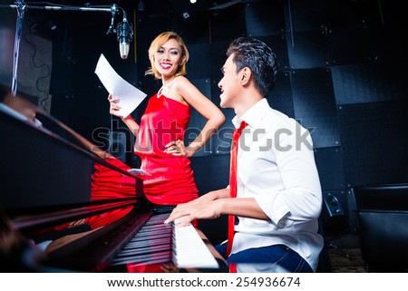 Asian professional singer and pianist working and discussing on new song in studio for composing and recording