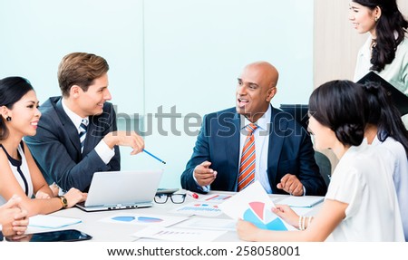 Diversity team in business development meeting with charts, Indian CEO and Caucasian executive crunching numbers, charts and figures on the desk