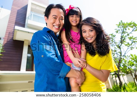 Asian Chinese family of parents and child standing proud in front of  modern home