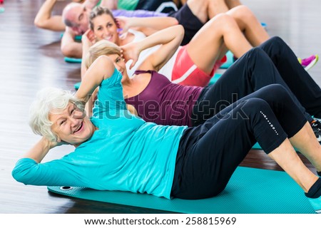 Group of senior people and young woman and men in fitness gym doing sit-ups on the floor