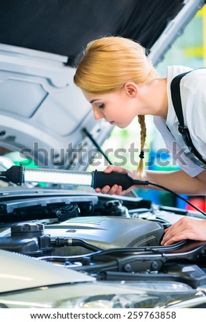 Female mechanic examine car engine with light in workshop
