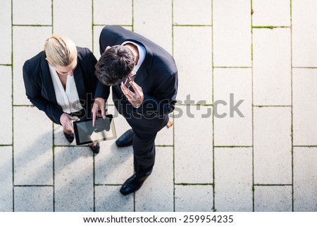 Business man and woman  with tablet computer standing on square, seen in top view