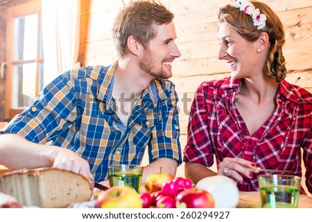 Man and woman eating food in mountain cabin in the alps with bread and cold cuts