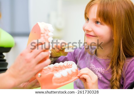 Female dentist explaining girl cleaning tooth with toothbrush on model